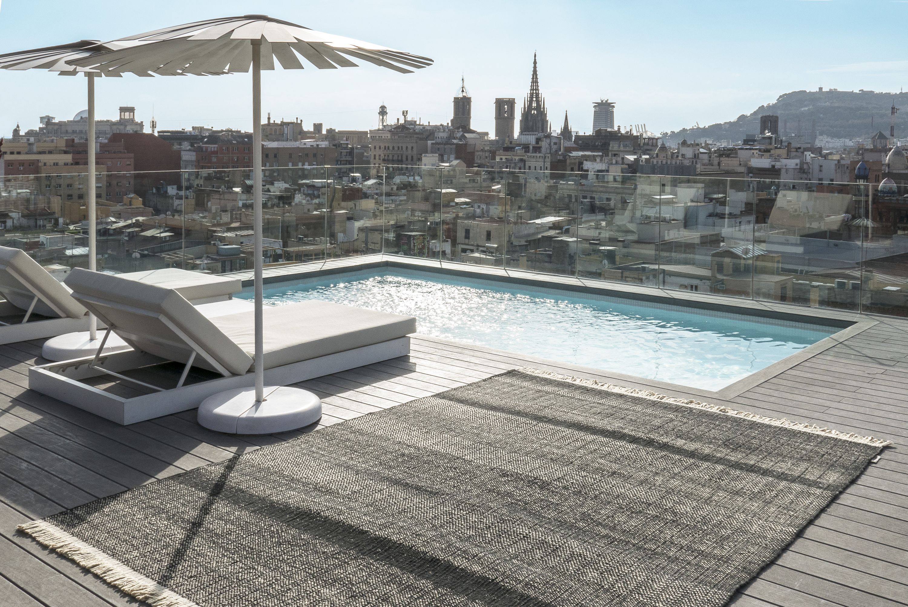 Nanimarquina Tres Outdoor Texture Teppich Schwarz 250x350 cm auf einer Dachterrasse mit Pool und Stadtblick.