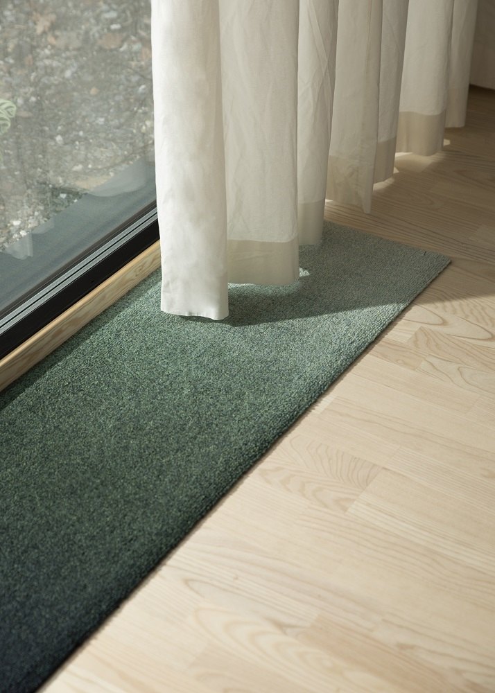 Nahaufnahme der grünen Heymat Ocean Fußmatte für Innen und Außen auf hellem Holzboden.