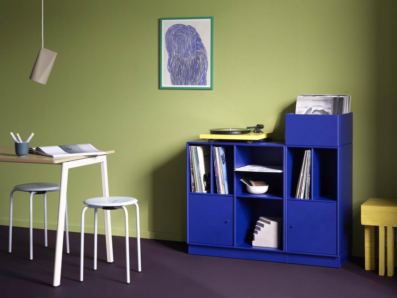 Blaues Montana Regal zur Schallplattenaufbewahrung mit Vinyl-Sammlung und gelbem Plattenspieler im Wohnzimmer.