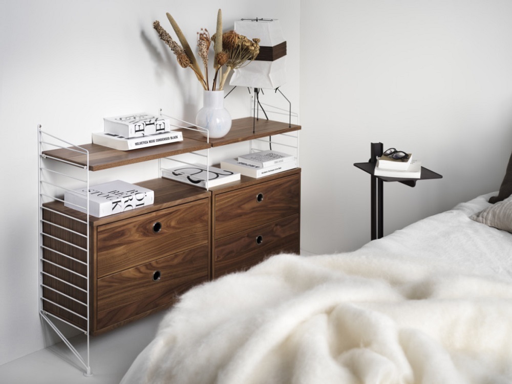 Museum Sidetable Beistelltisch von String Furniture neben einem Bett, höhenverstellbar, mit Regalen und Schubladen.