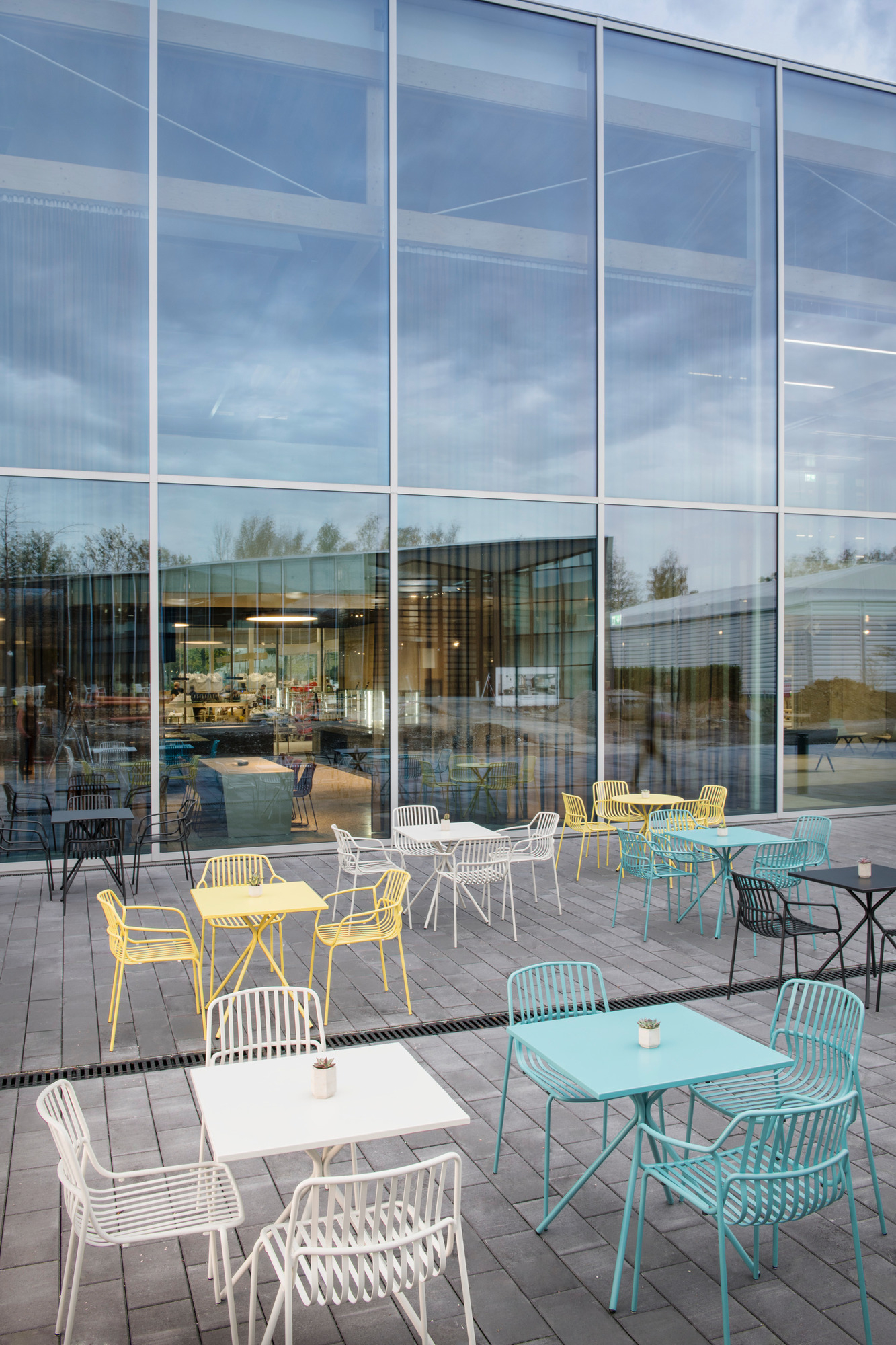 Quadratische Crona Steel Bistrotische von Brunner in verschiedenen Farben für den Außenbereich, vor Glasfassade.