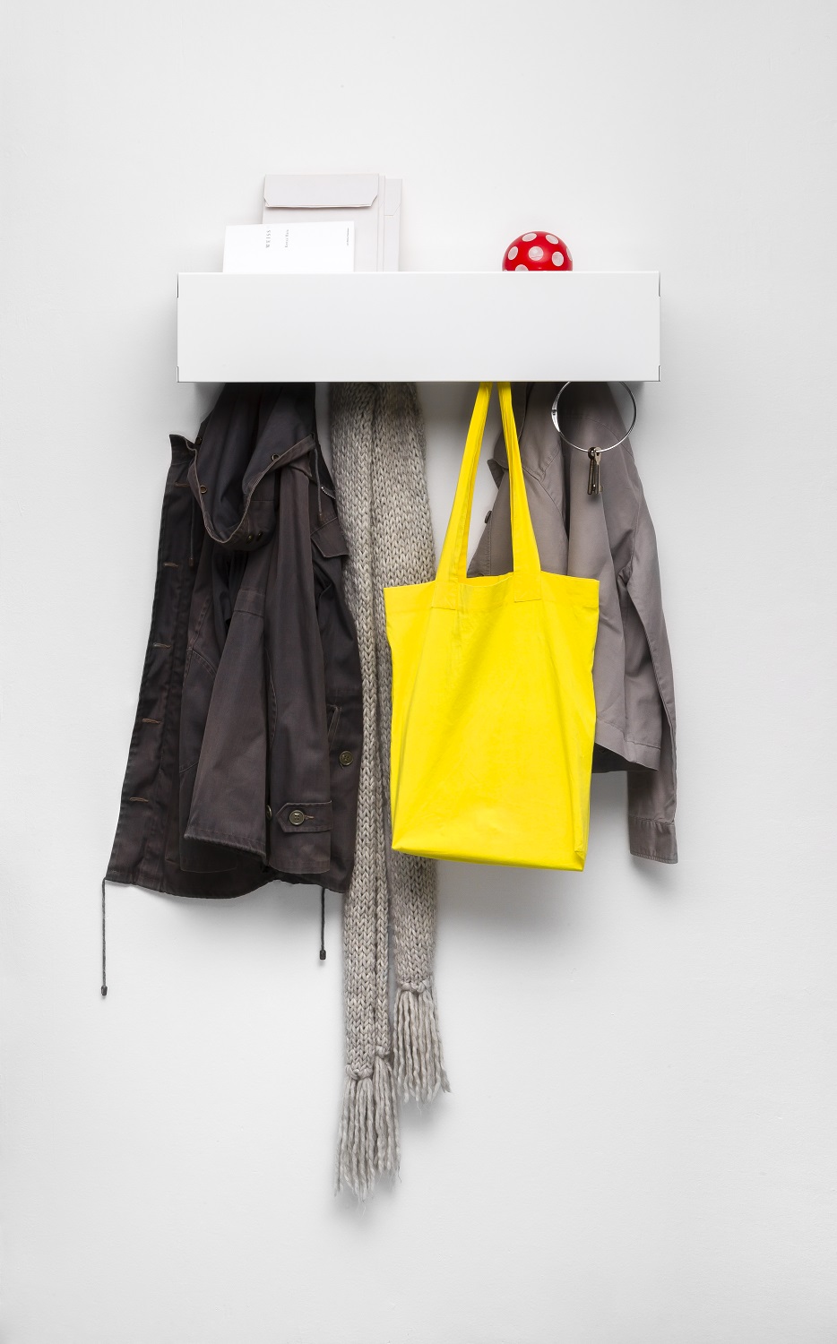 Weiße Müller Möbelwerkstätten CR Linea1 Wandgarderobe mit Jacken, Schal und gelber Tasche an einer weißen Wand.