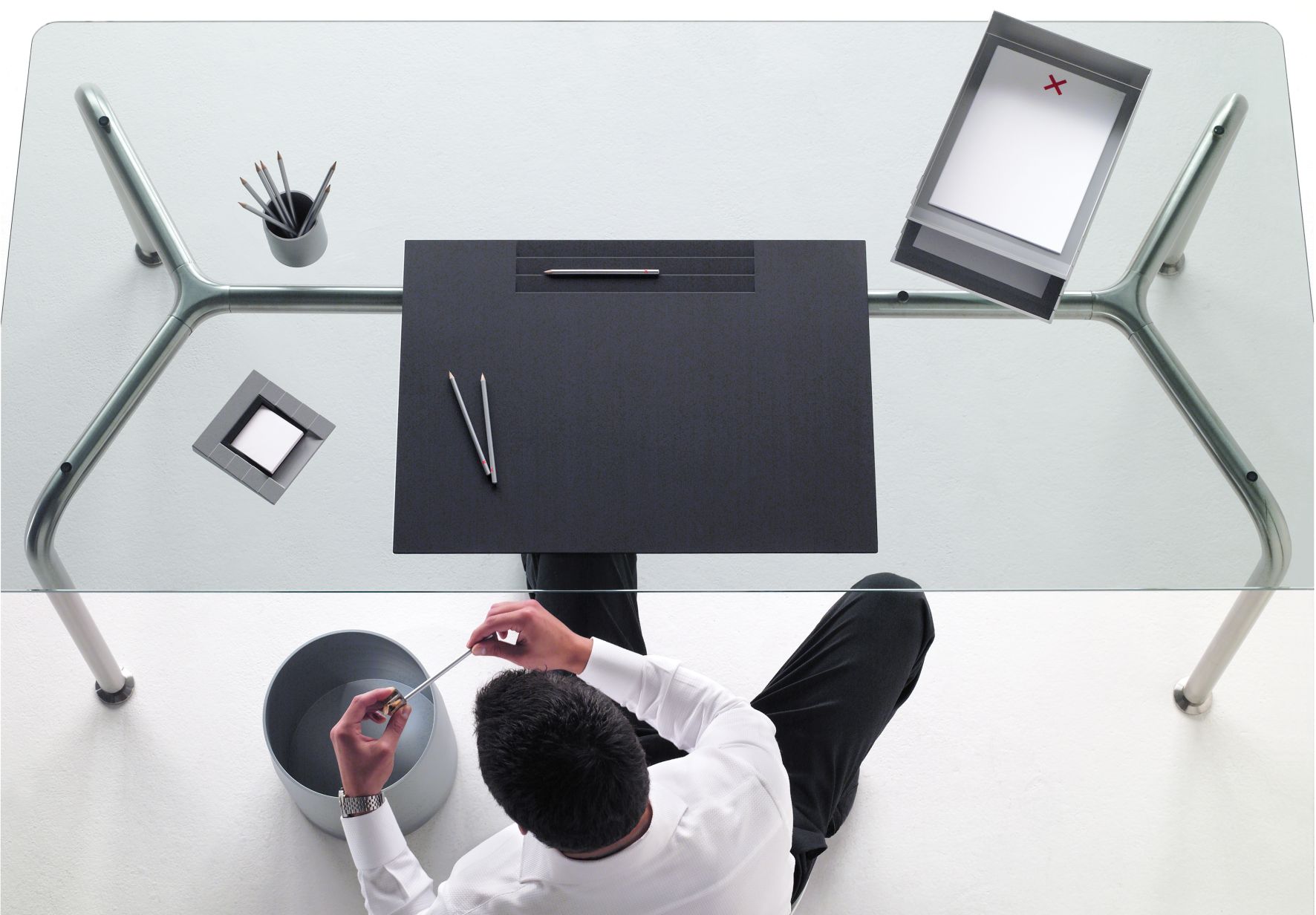 Ansicht von oben: Mann leert Rexite Papierkorb unter einem Glastisch mit Büroartikeln.