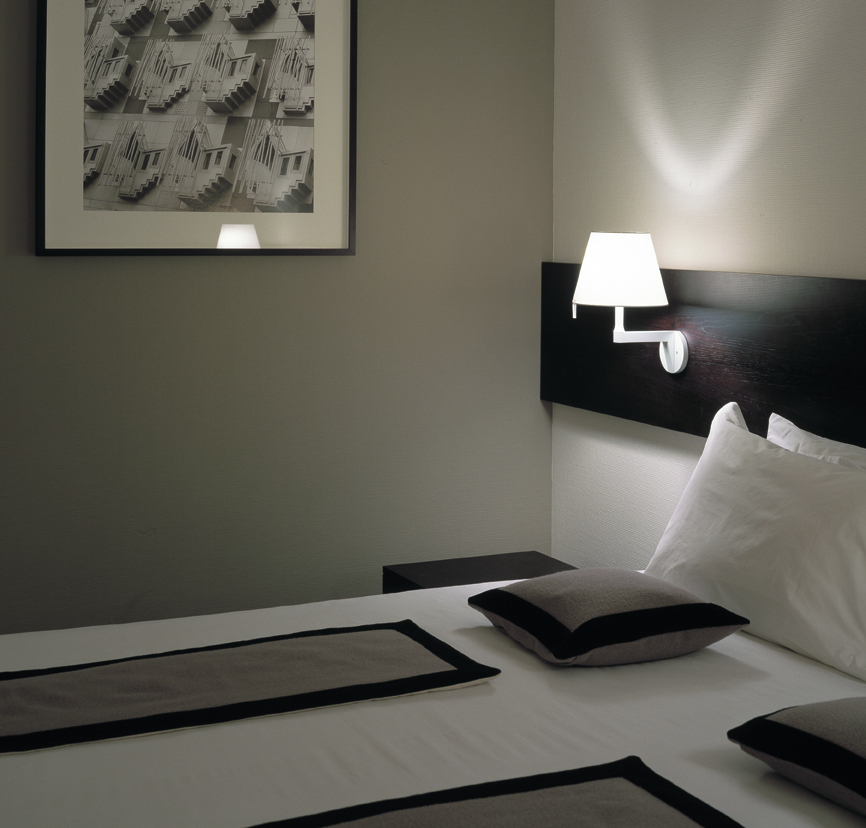 Nahaufnahme einer weißen Melampo Wandleuchte von Artemide über einem Bett.