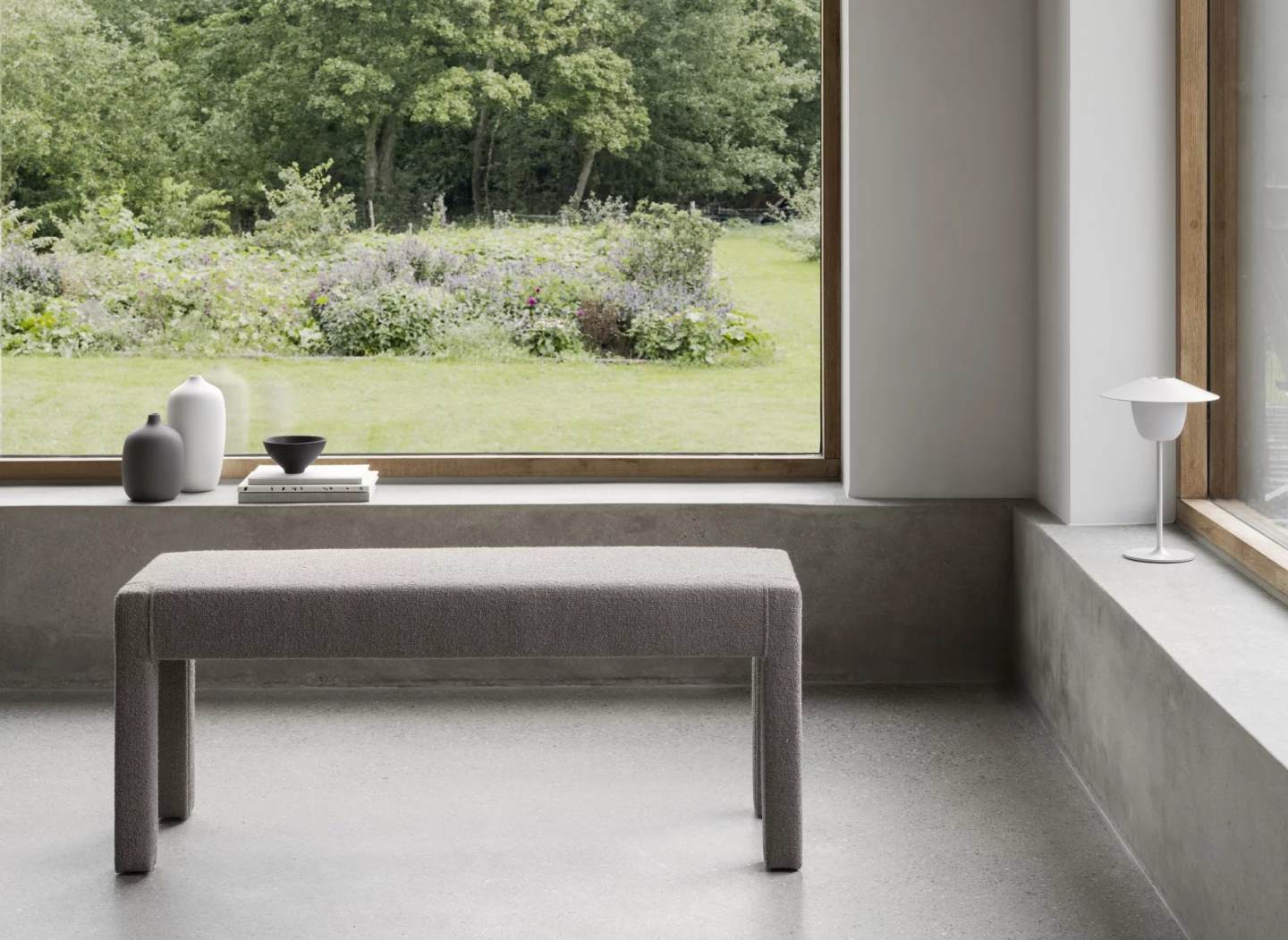 Graue Sitta Bank von Blomus vor Fenster mit Gartenblick. Moderne Sitzbank für zwei Personen.