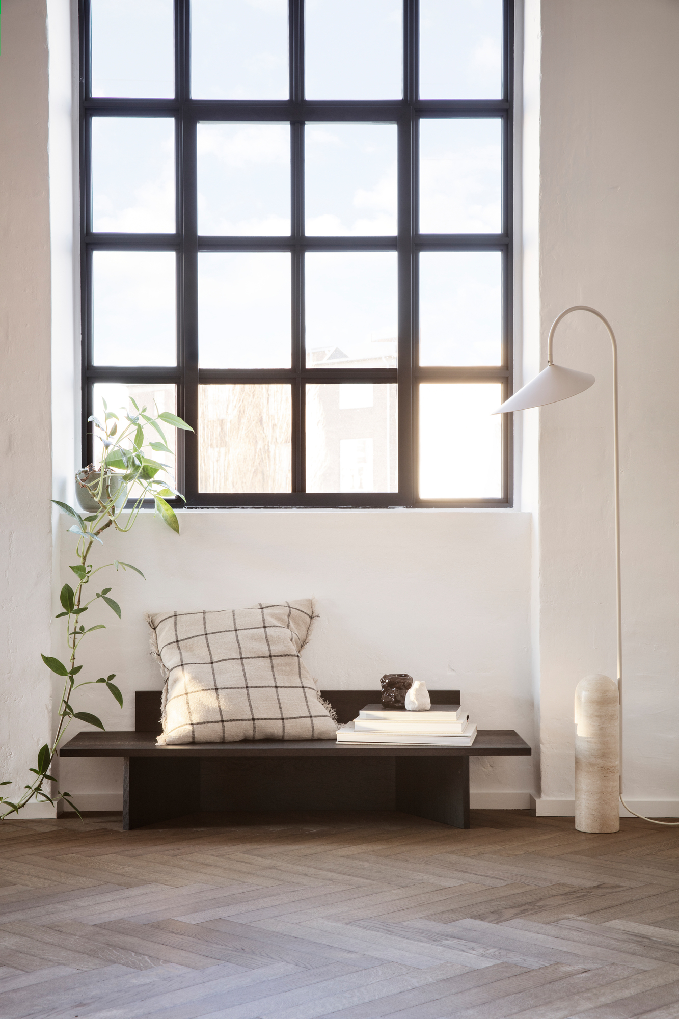 Oblique Bank von Ferm Living aus dunklem Holz mit Kissen und Dekoration vor Fenster.