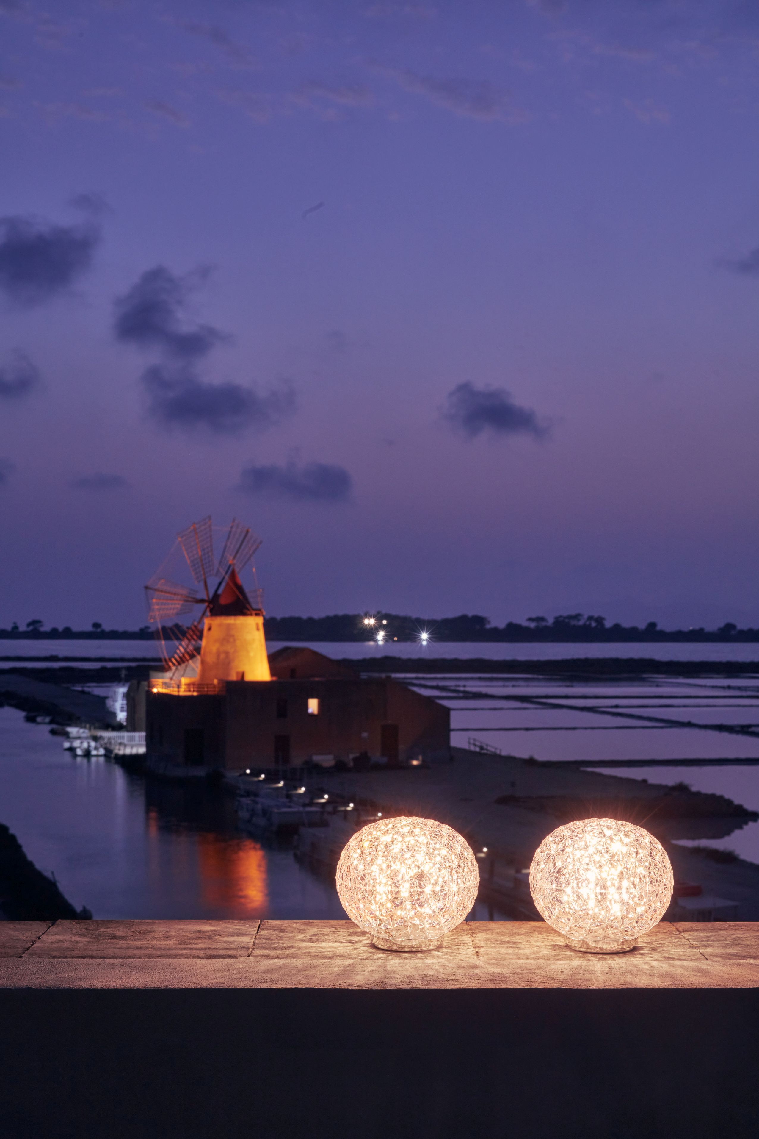 Zwei Kartell Planet Tischleuchten in Rauch vor einer malerischen Landschaft im Abendlicht.