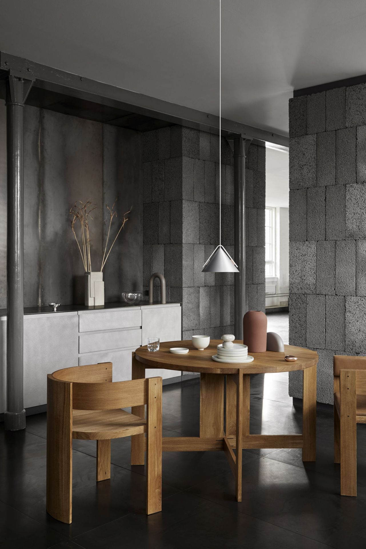 Runder Holztisch mit Stühlen und Pendelleuchte in modernem Esszimmer mit Betonwand und minimalistischer Dekoration.