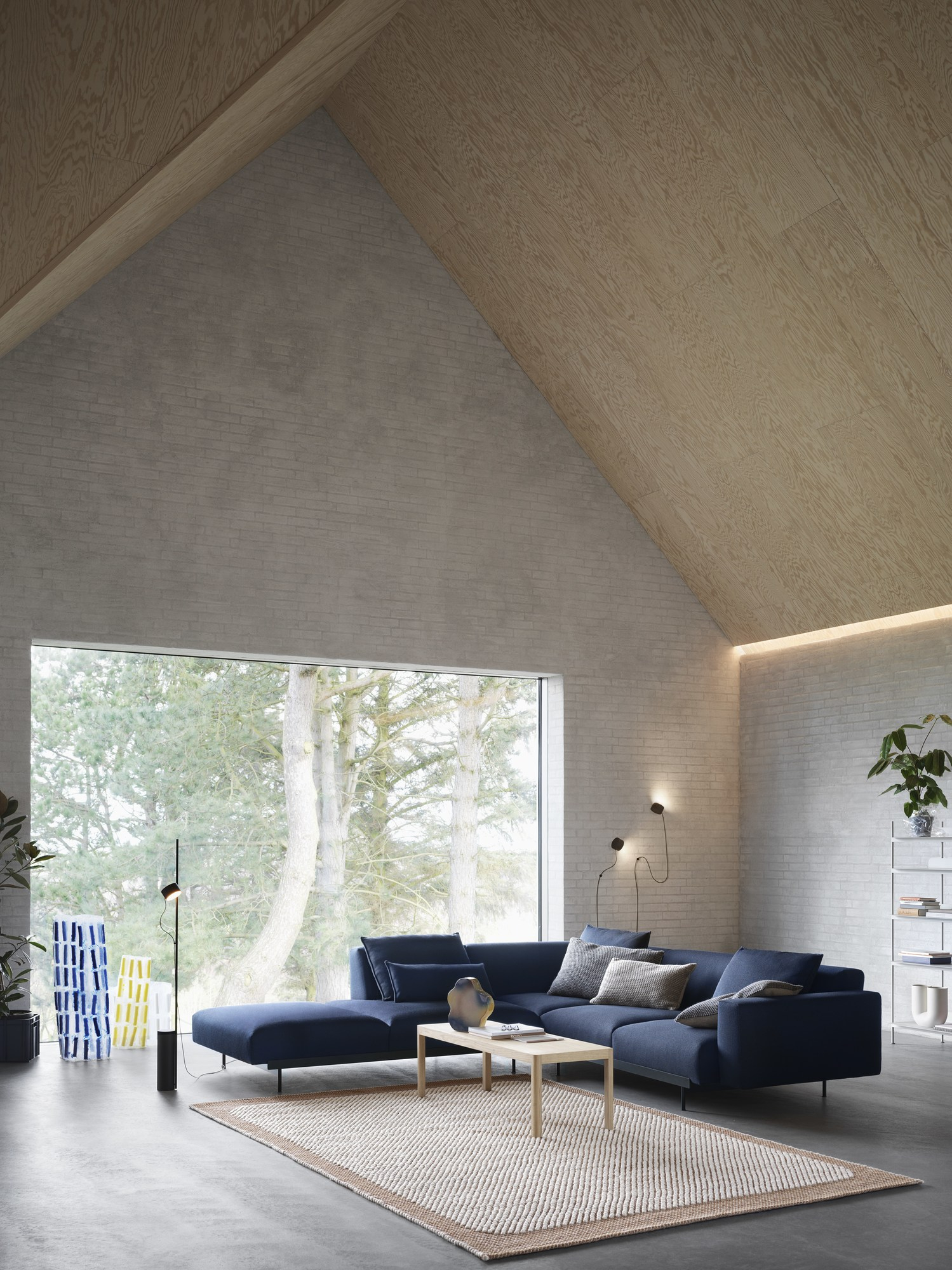 Wohnzimmer mit Muuto Post Wall Lamp Wandleuchten und blauem Ecksofa vor großem Fenster.