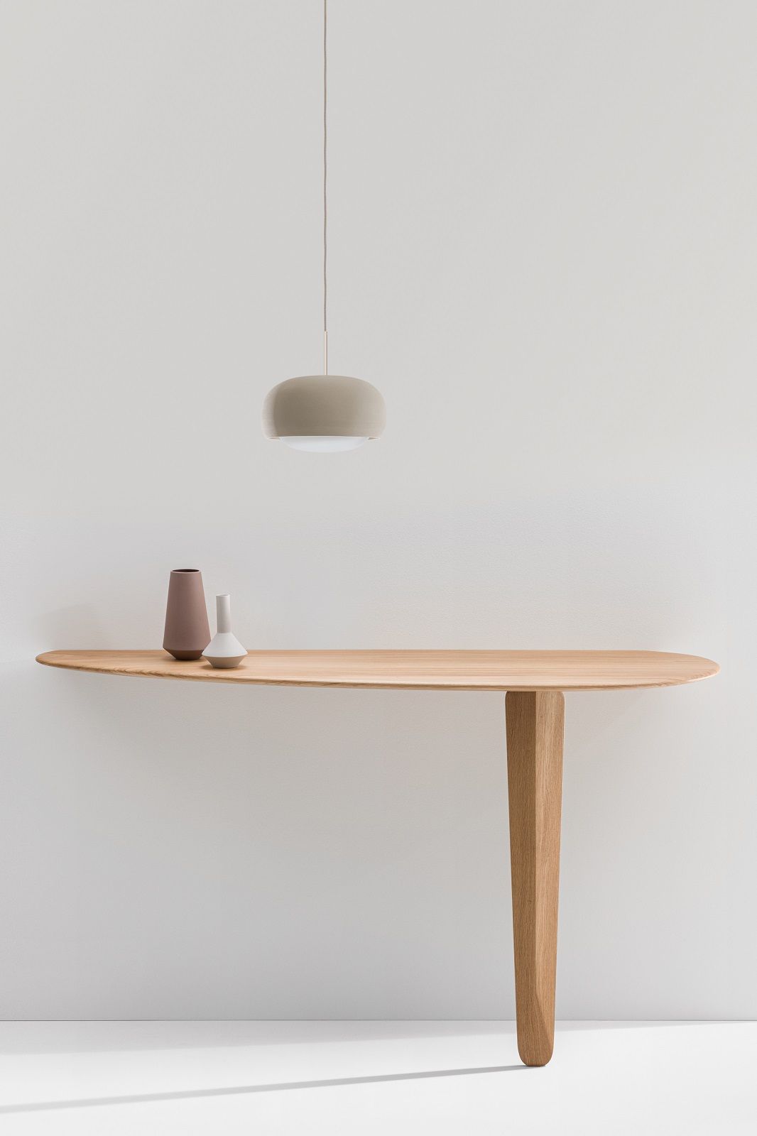 Kuyu Console Tisch: Asymmetrischer Konsoltisch aus Holz mit Vasen und Hängelampe vor weißer Wand.