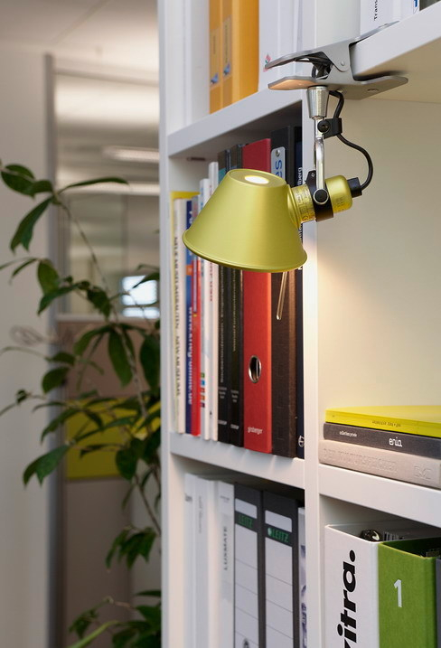 Nahaufnahme der gelben Artemide Tolomeo Pinza Klemmleuchte, befestigt an einem weißen Bücherregal mit Ordnern.
