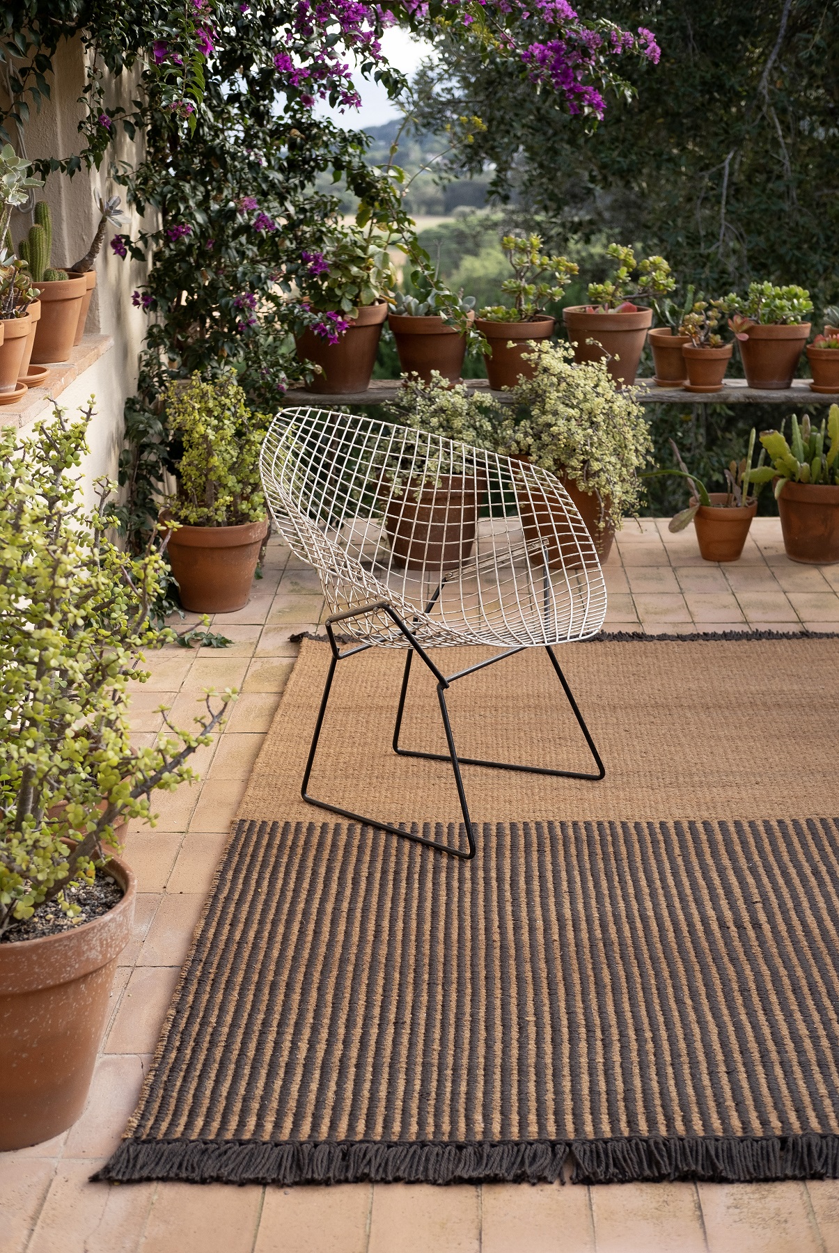Nanimarquina Garden Outdoor Teppich in Schwarz mit Streifenmuster auf einer Terrasse mit Pflanzen.