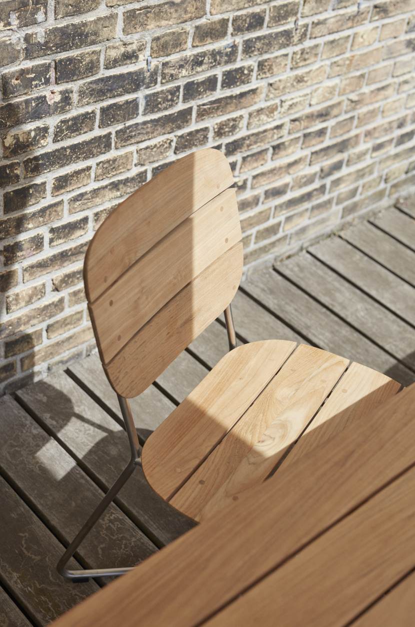Lilium Chair Stuhl von Skagerak: Outdoor-Stuhl aus Teakholz mit Stahlgestell vor Backsteinwand.