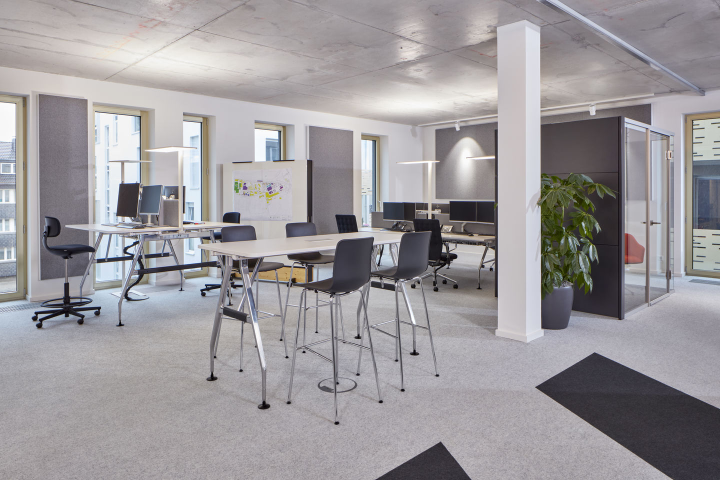 Heller Büroraum mit Stehtischen und einem schwarzen Rookie High Bürodrehstuhl von Vitra.