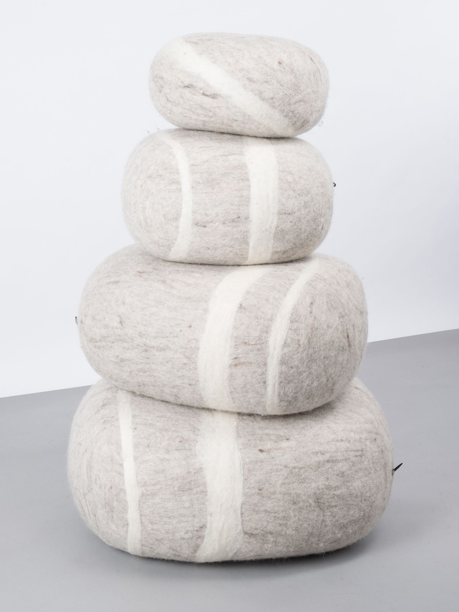 Filz Kieselstein Hocker Béla: Vier gestapelte, graue Filzkissen mit weißen Streifen als Sitzgelegenheit.