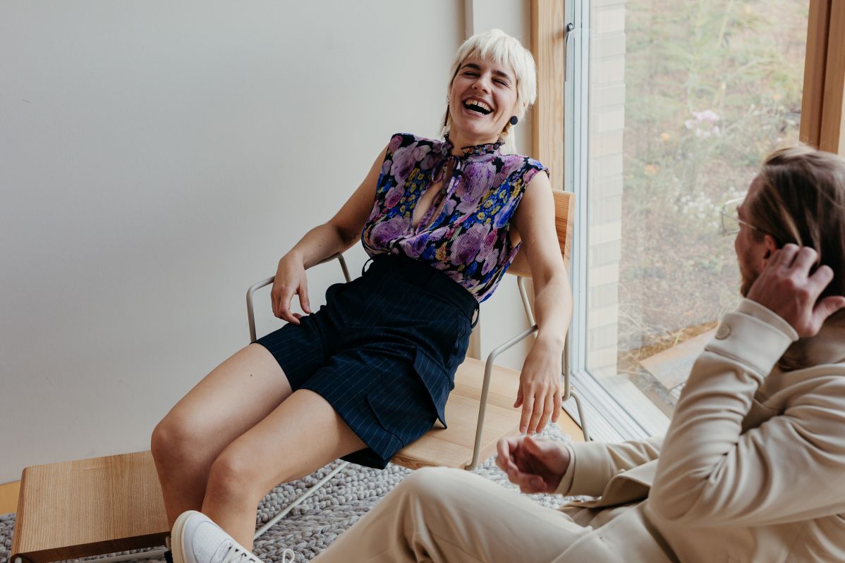 Frau lacht entspannt im D:008 Loungechair von Fuchs & Habicht, Waldgrün, mit Armlehnen.
