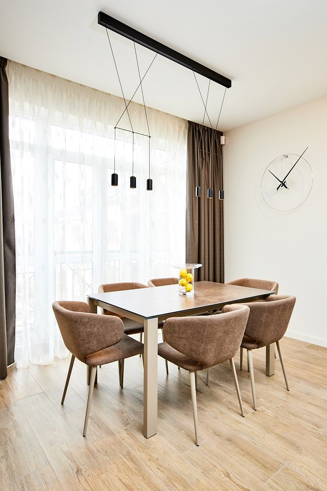 Esszimmer mit New Anda Clock Wanduhr, Esstisch und Stühlen in modernem Design.