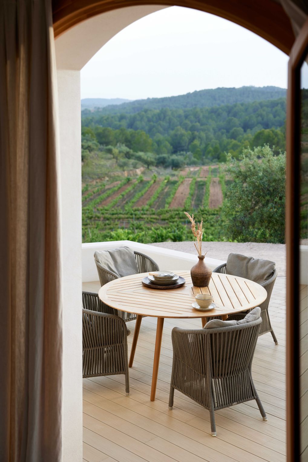 Derby Outdoor Stuhl Taupe von Cane-Line um einen runden Holztisch auf einer Terrasse.