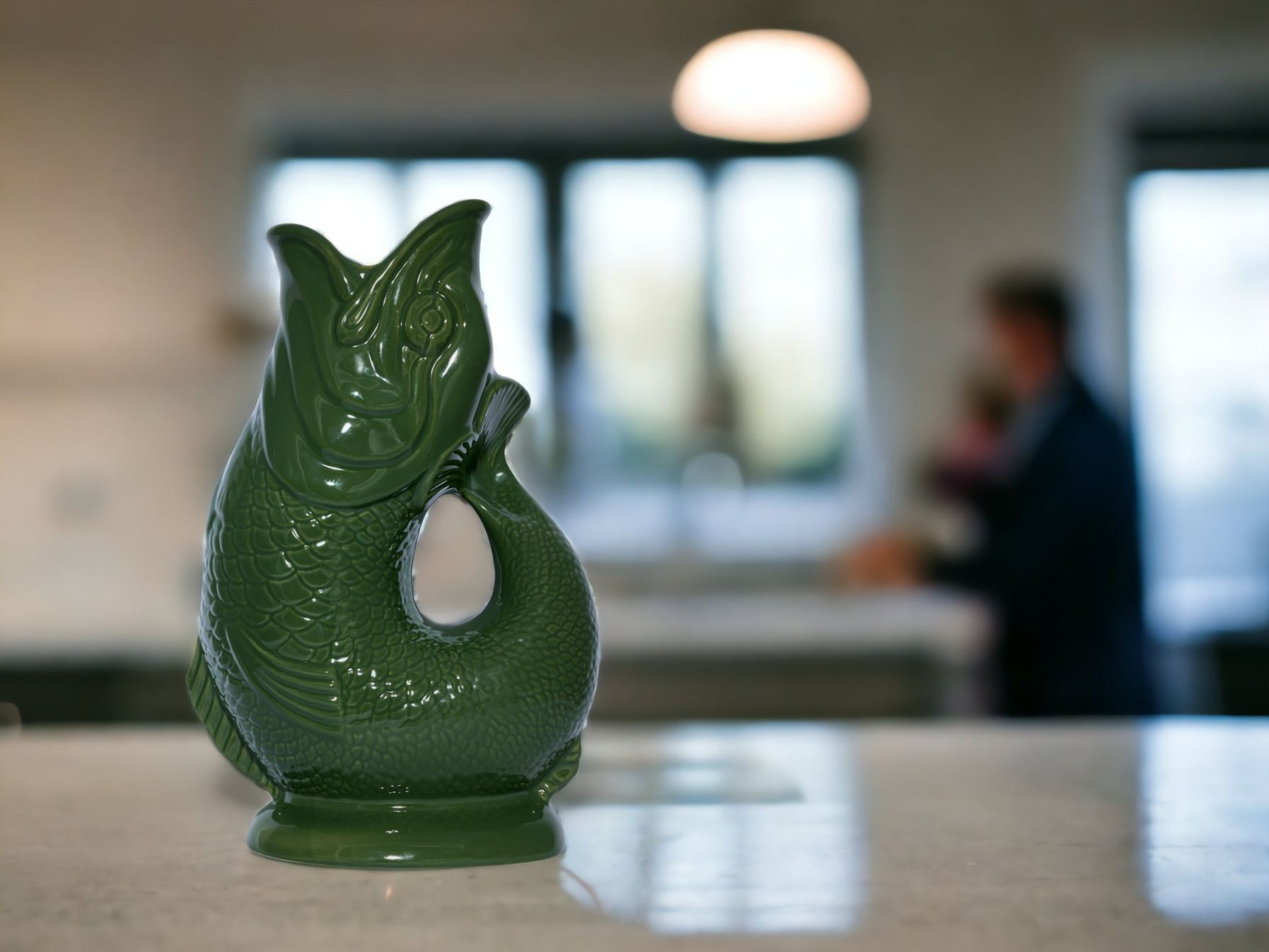 Dunkelgrüne Gluckigluck Fischkaraffe XL auf einer Küchentheke, dekorative Keramikvase in Fischform.