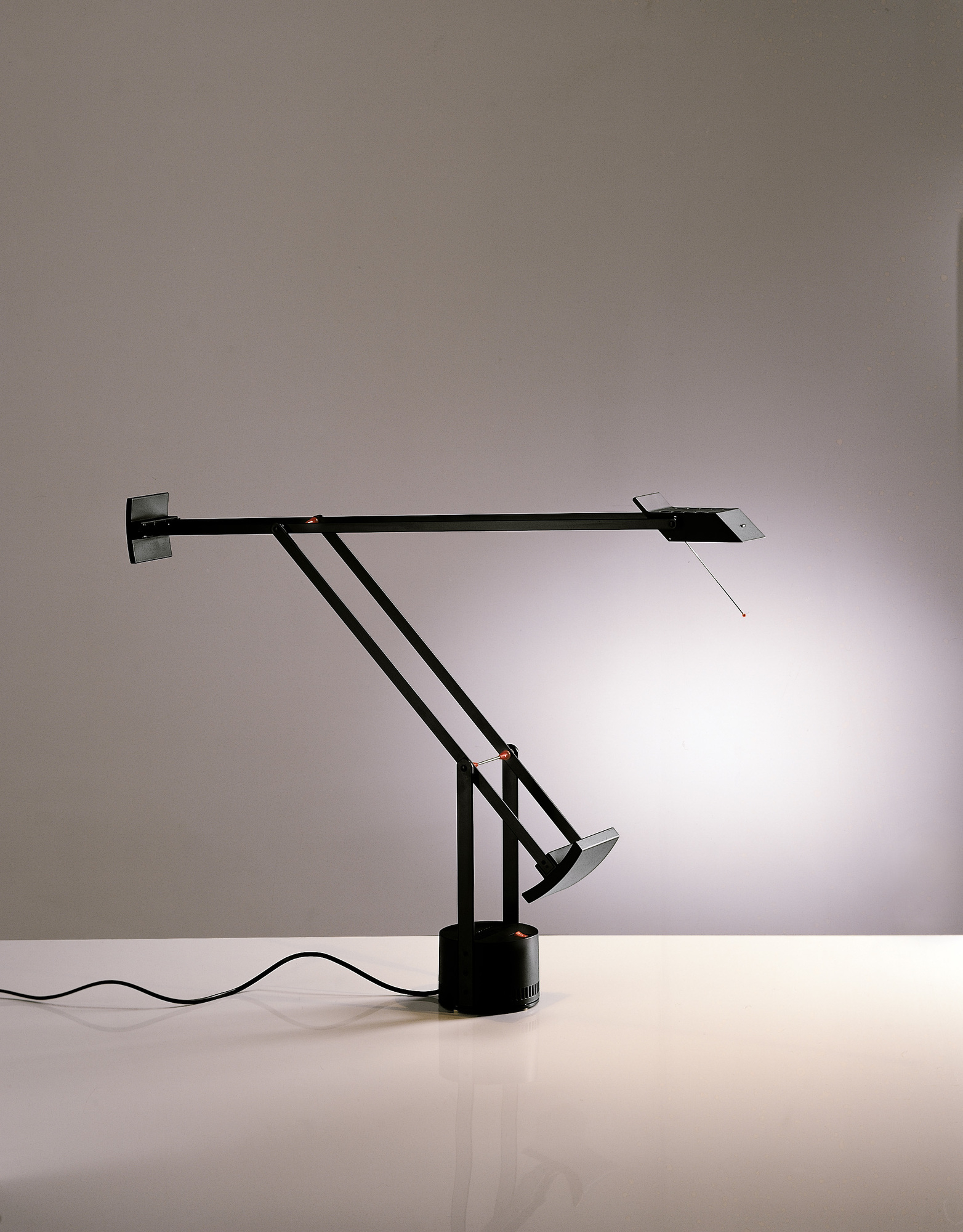 Schwarze Tizio Tischleuchte von Artemide mit verstellbarem Arm und Lichtkegel auf einem weißen Tisch.