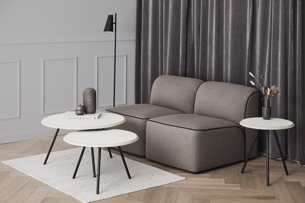 Wohnzimmer-Szene mit Cono Stehleuchte von Woud, grauem Sofa und weißen Beistelltischen.