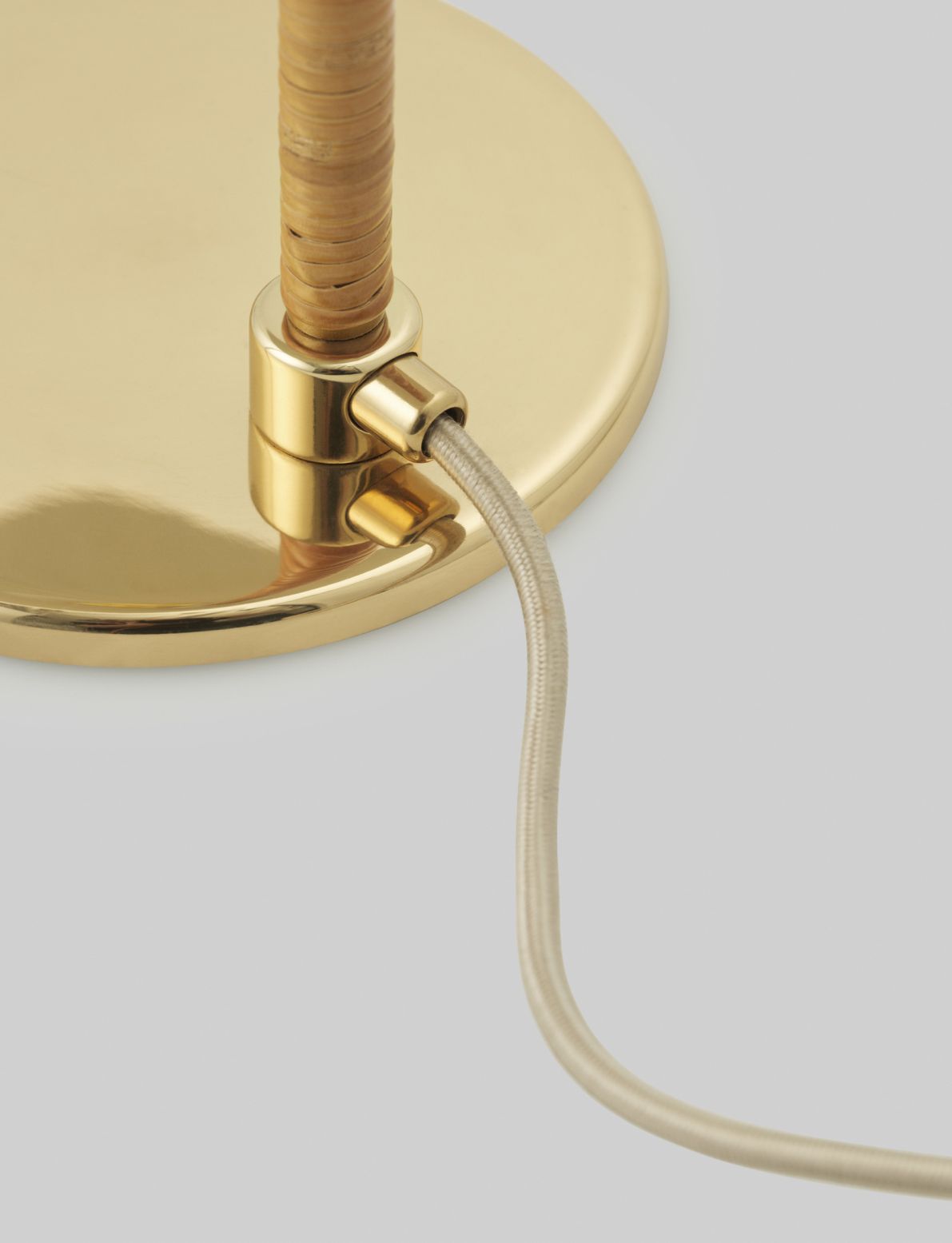 Detailaufnahme der Gubi 5321 Tischleuchte: Goldener Fuß, Rattanstiel und Textilkabel. Design-Tischlampe für Wohnzimmer.