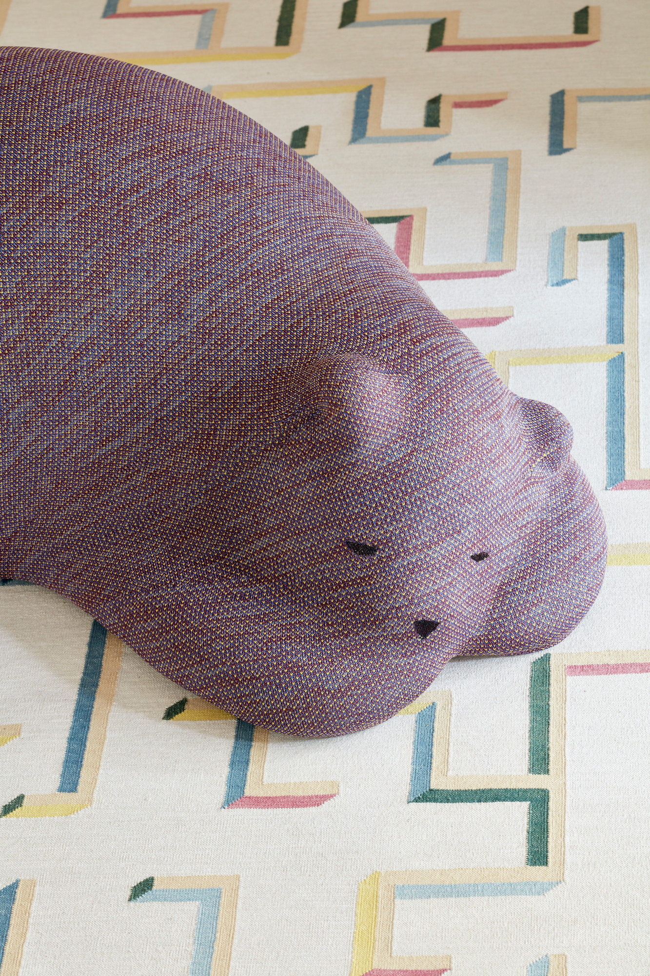 Nahaufnahme des Vitra Resting Bear Stofftieres auf einem Teppich mit geometrischen Mustern.