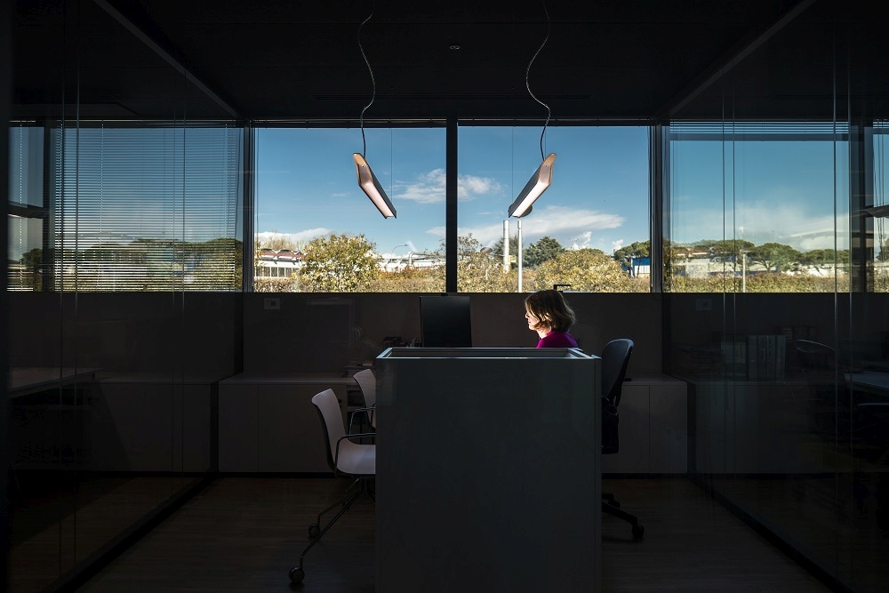 Moderne Troag LED Hängeleuchte von Foscarini über einem Schreibtisch in einem Büro mit großer Fensterfront.