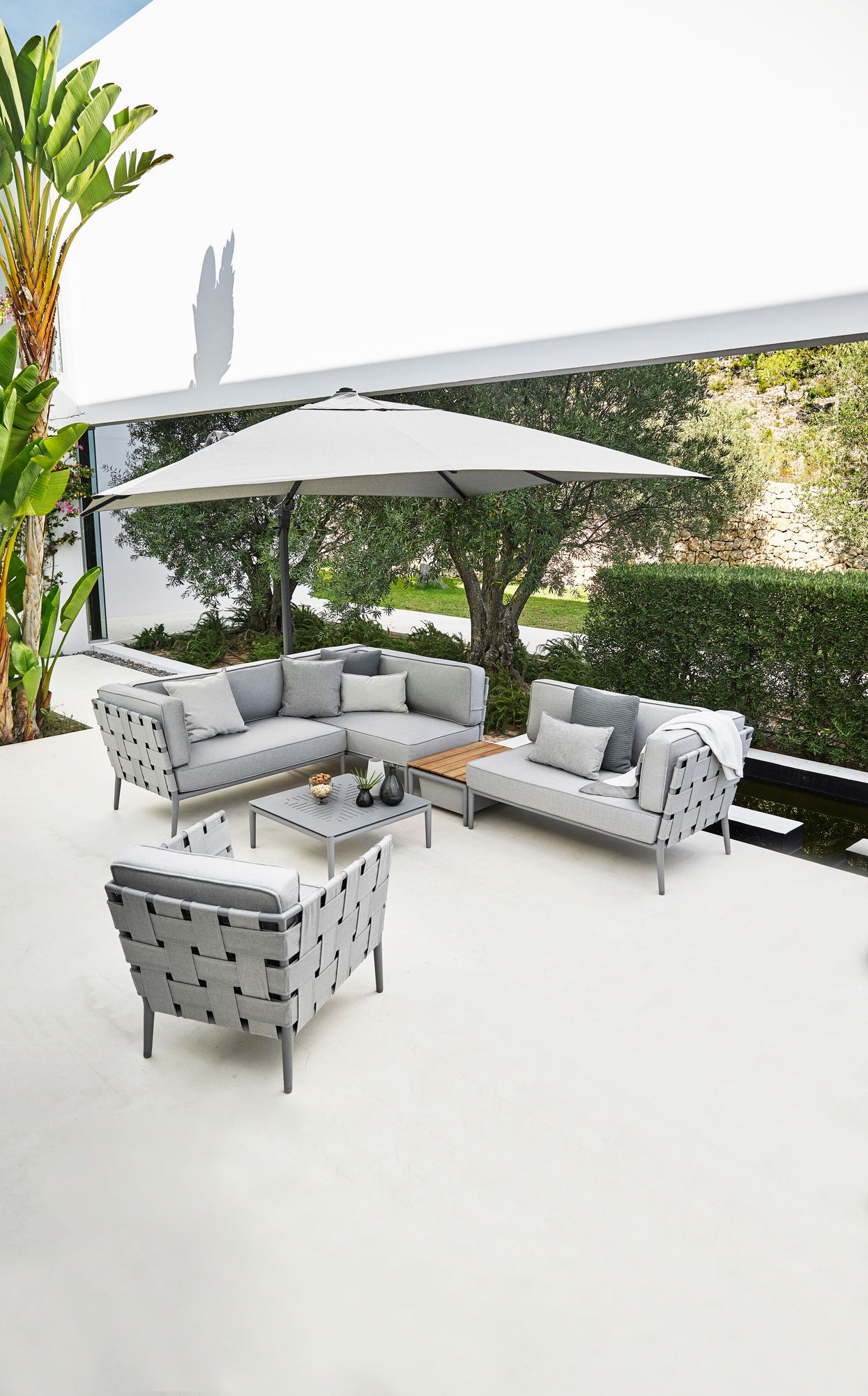 Heller Conic AirTouch Loungesessel von Cane-Line im Outdoor-Bereich mit Lounge-Möbeln und Sonnenschirm.