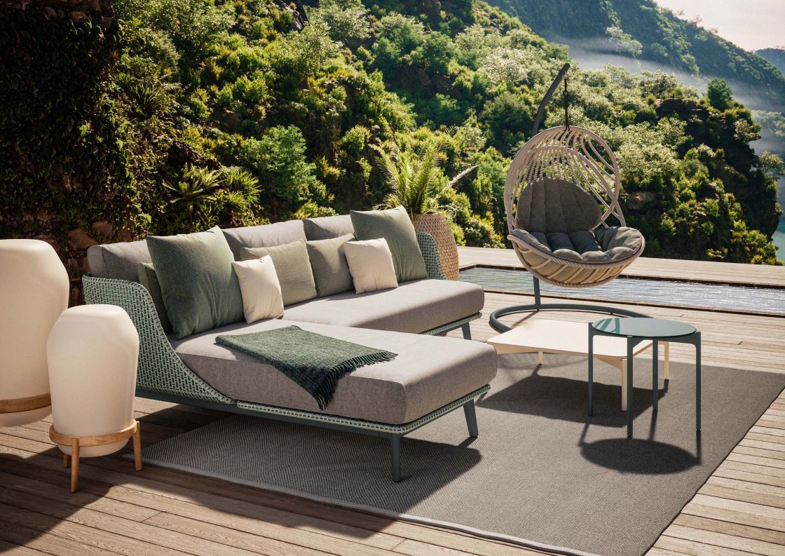 Outdoor-Lounge mit Sofa, Hängesessel, Teppich und Beistelltischen auf einer Holzterrasse mit Pool und üppigem Grün.
