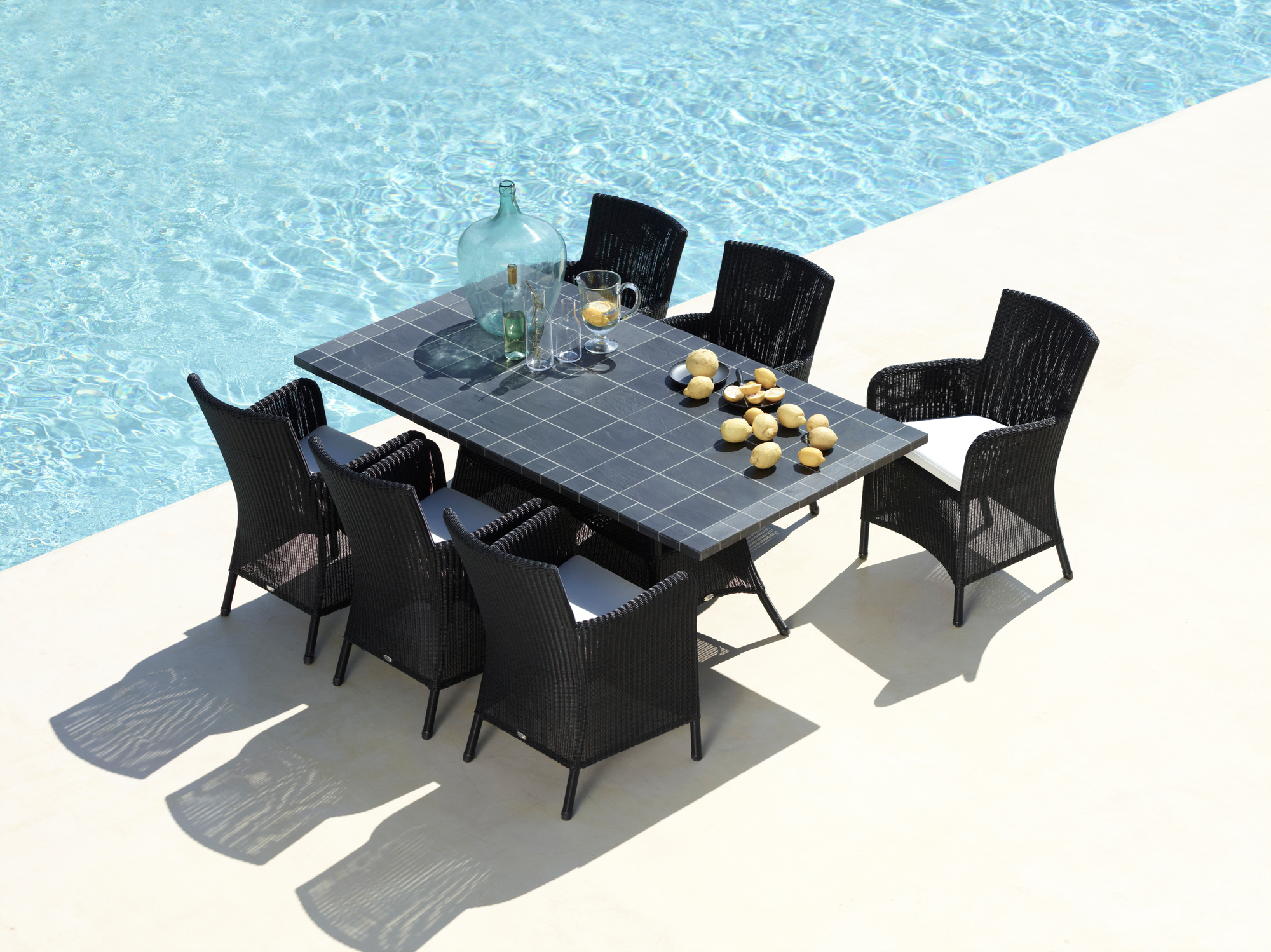 Hampsted Outdoor Sessel von Cane-Line, schwarz, mit Esstisch und Pool im Hintergrund.