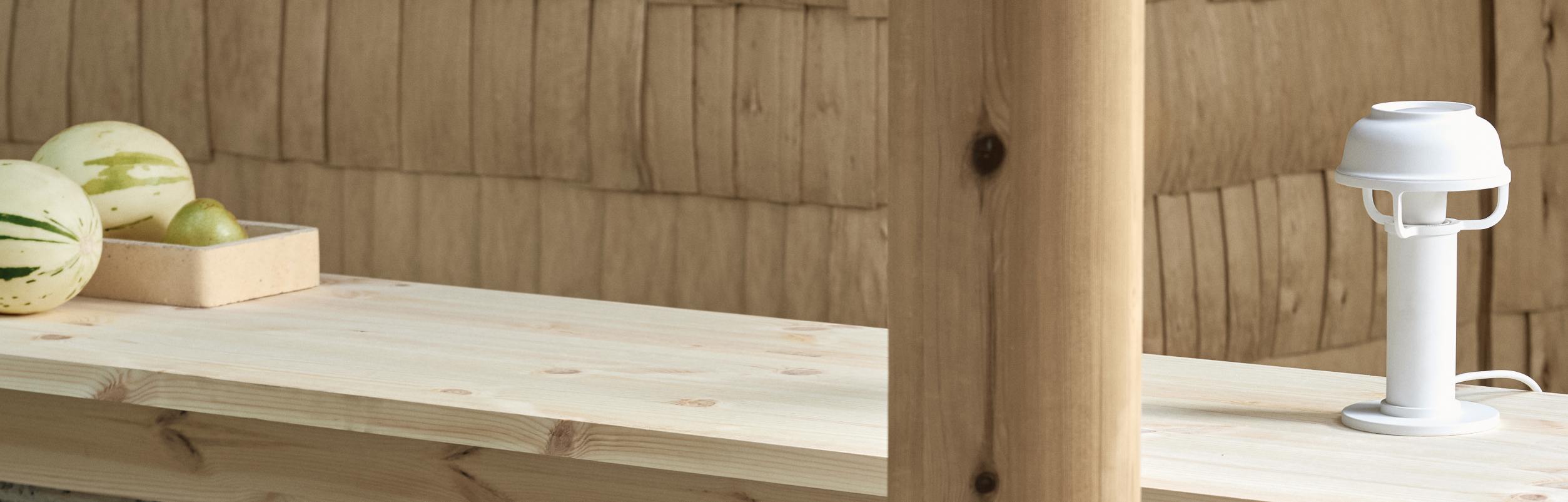 Weiße Kori Tischleuchte von Artek auf einem Holztisch mit Früchten. Designleuchte für Wohnraum.