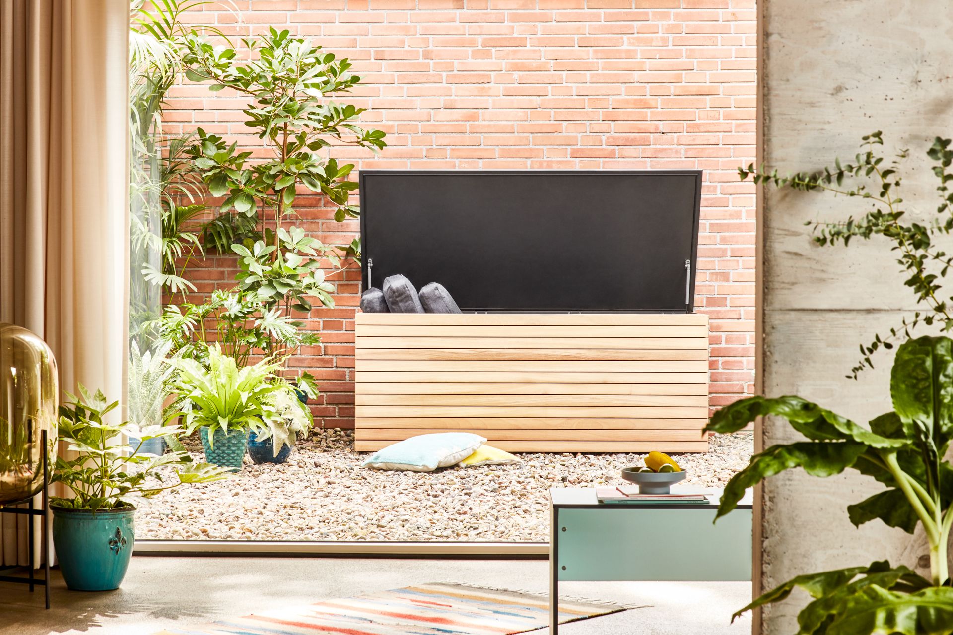 Geöffnete Forte Kissentruhe von Conmoto aus Lärche und Anthrazit mit Kissen im Garten.