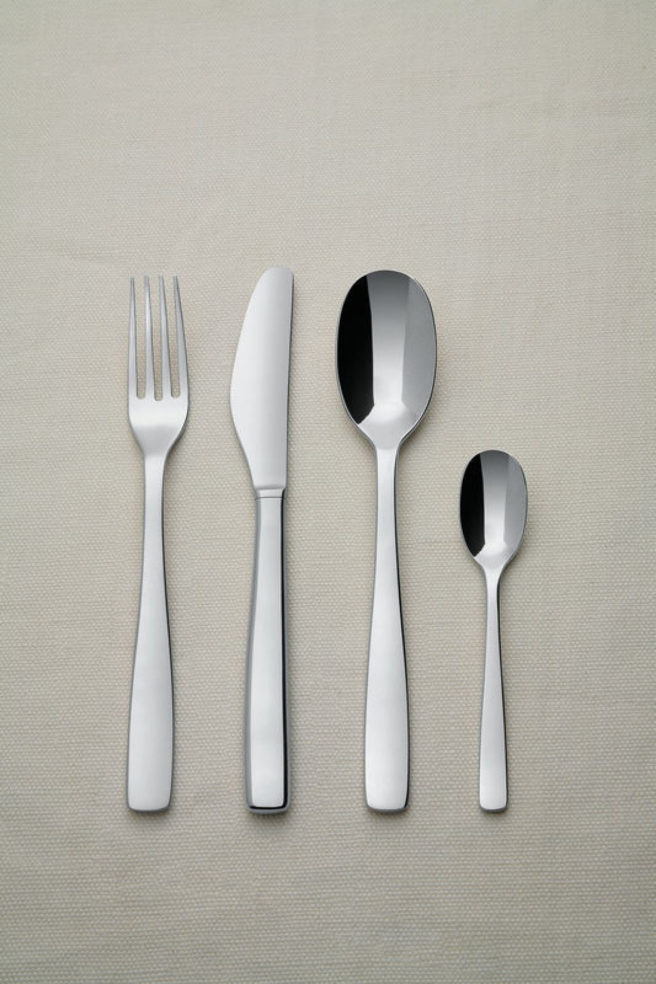 Edelstahl Besteckset: Messer, Gabel, Esslöffel und Teelöffel auf beigem Hintergrund, modernes Design.