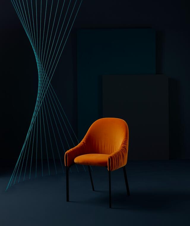 Orangefarbener Celine Armchair Sessel von Freifrau Manufaktur mit schwarzen Beinen vor dunklem Hintergrund.