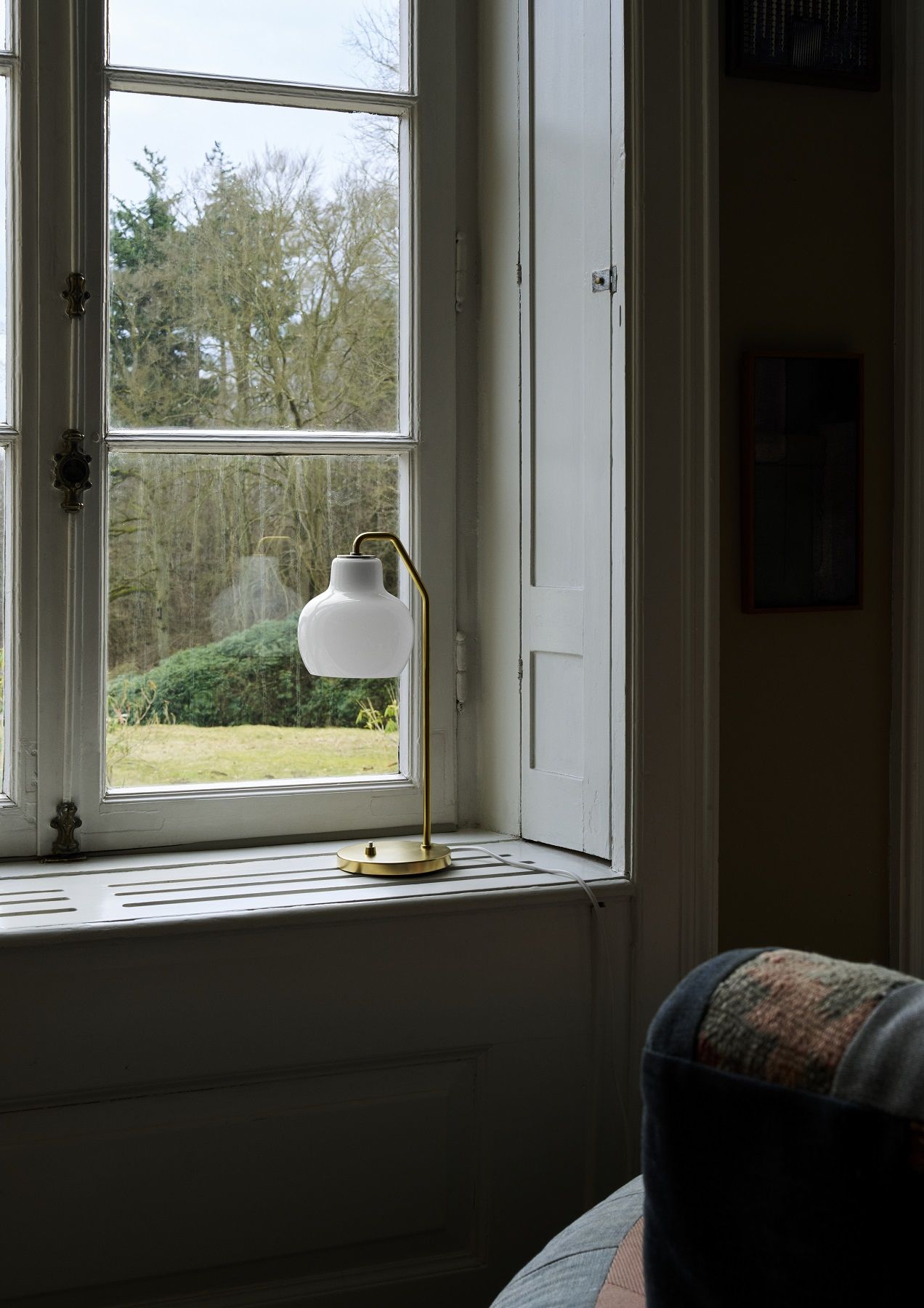 VL Ring Crown Tischleuchte von Louis Poulsen auf einer Fensterbank mit Blick auf einen Garten.