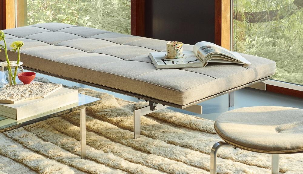 Beiger PK33 Hocker von Fritz Hansen mit gesteppter Sitzfläche und Stahlgestell im Wohnzimmer.