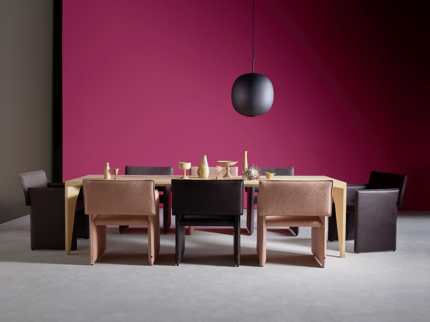 Esstisch mit Noto Stühlen von Wangen Cor in Braun- und Rosatönen vor pinkfarbener Wand.