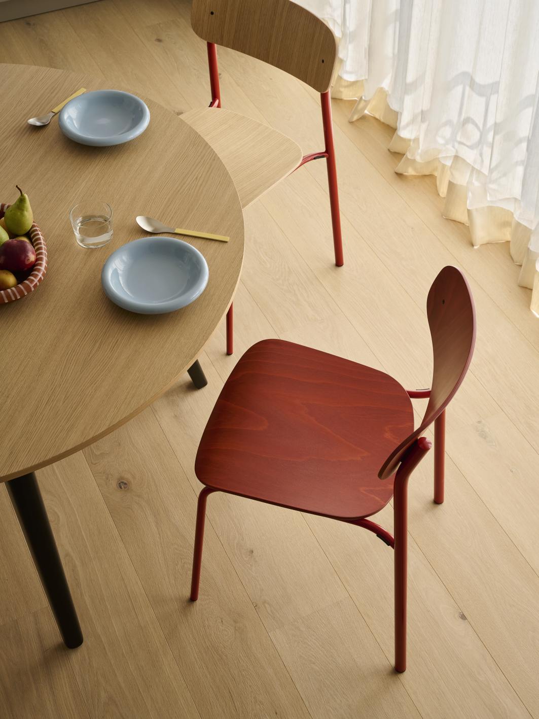 Nahaufnahme von zwei Stahlrohrstühlen, einer davon rot, am Holztisch. Thonet Stuhl Designmöbel.