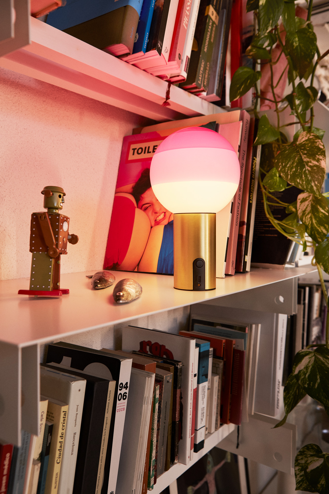 Marset Dipping Light Portable Akkuleuchte Bernstein-Messing auf Regal mit Büchern und Dekoration. Tischleuchte mit warmem Licht.