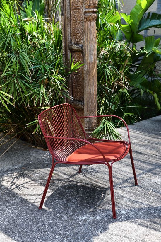 Roter Hiray Stuhl von Kartell für den Außenbereich mit Sitzkissen vor tropischer Kulisse.