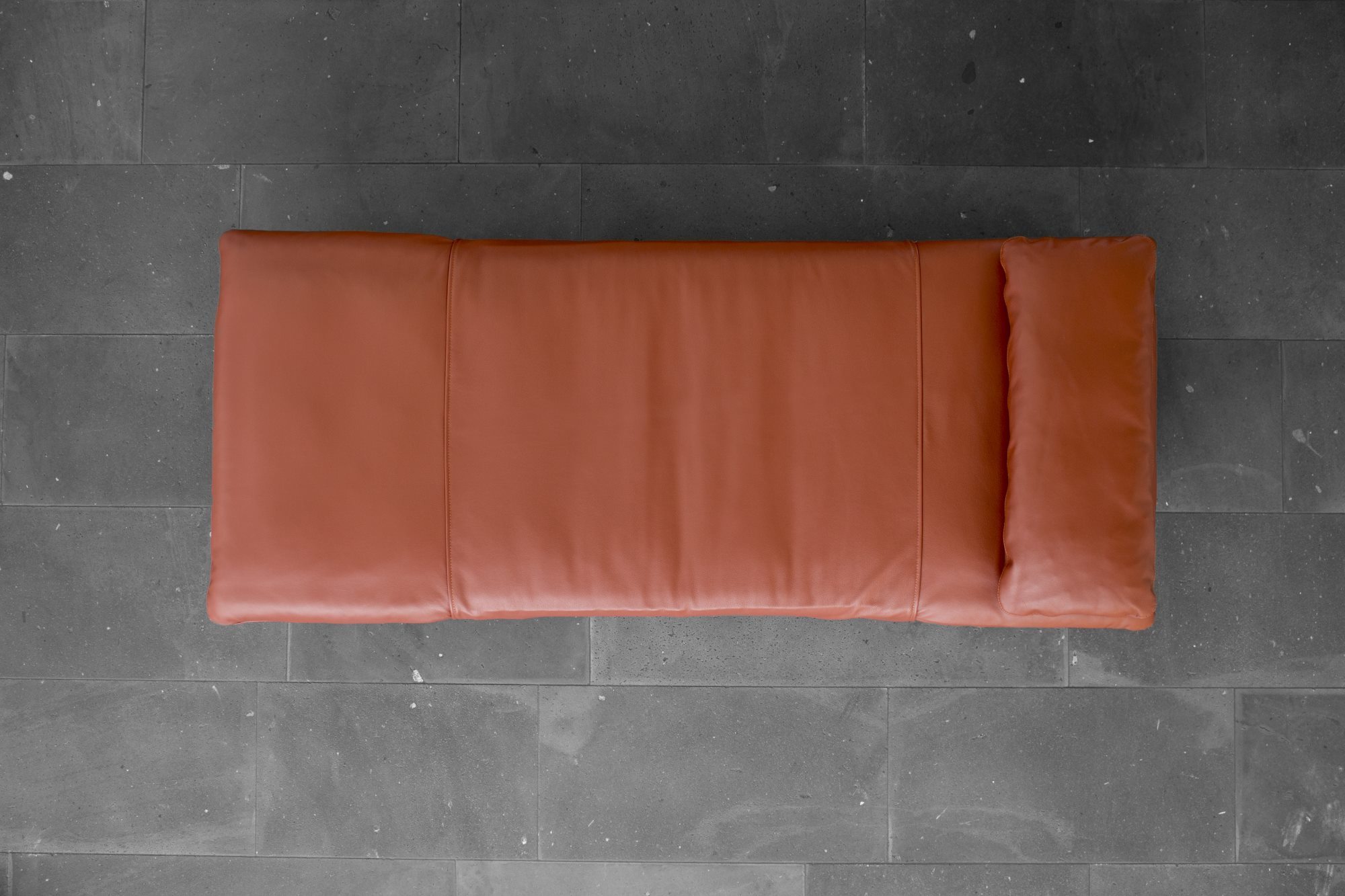 Draufsicht: Terrakottafarbenes Paletten Daybed mit Kissen auf grauem Steinboden. Gemütliche Outdoor-Lounge für Garten und Terrasse.