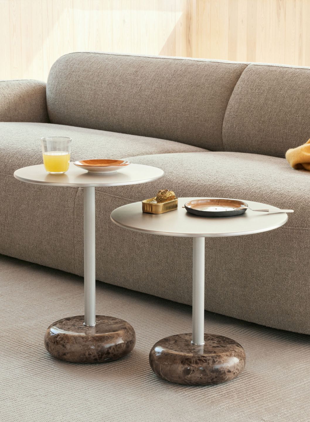 Zwei Northern Ton Beistelltische mit Marmorfuß und grauem Sofa im Hintergrund, einer mit Getränk und Teller.