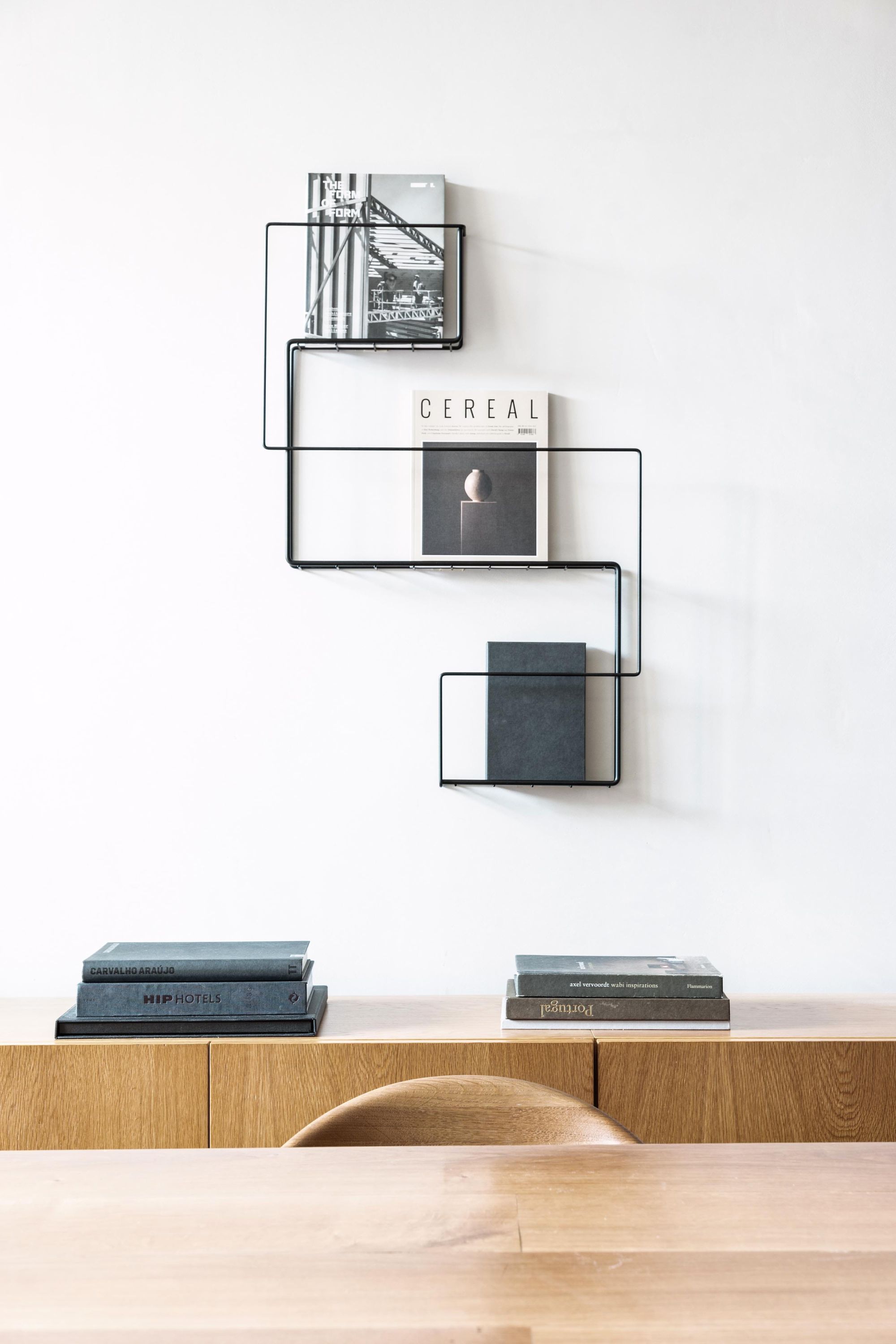 Schönbuch Revue Wand-Zeitungsständer aus schwarzem Metall mit Zeitschriften an einer weißen Wand. Minimalistisches Design.