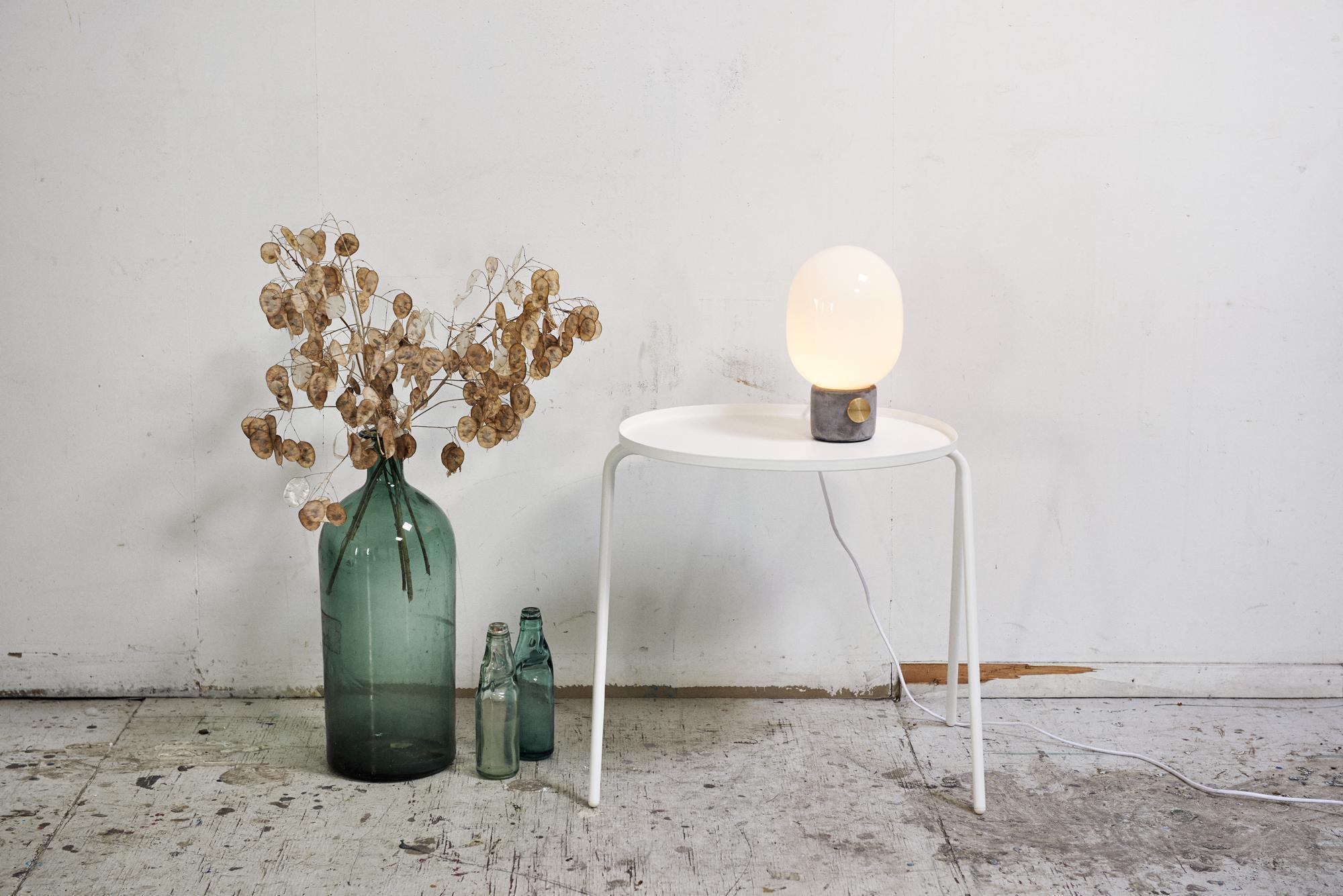 JWDA Concrete Lamp: Tischleuchte mit Betonfuß und opalweißem Glas auf weißem Tisch.