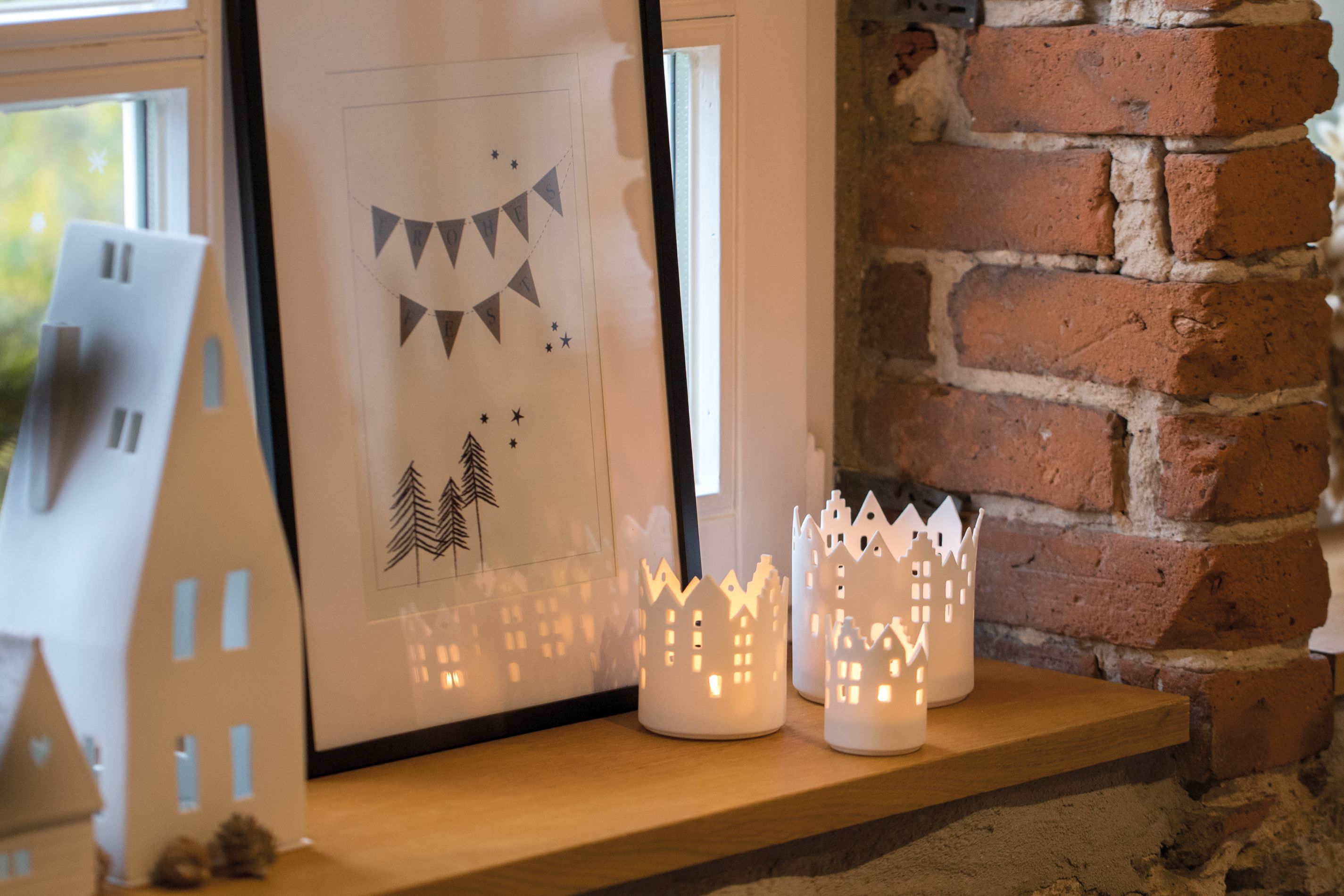 Drei weiße Stadtlicht Rathausplatz Räder Teelichthalter auf einem Holzregal, neben einem Fenster und Backsteinmauer.
