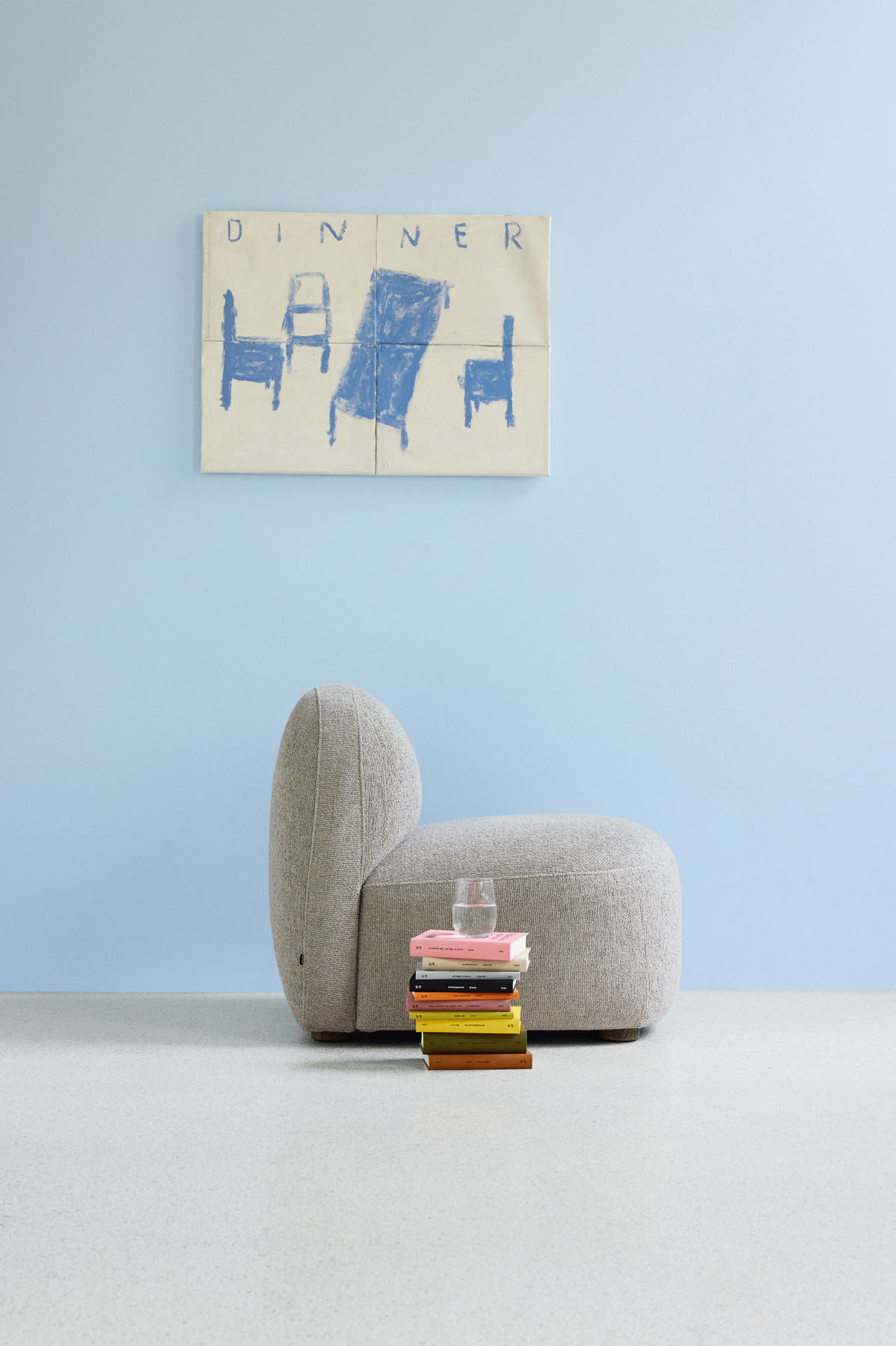 Beiger Gem Loungesessel von Northern mit Büchern und Wasserglas vor hellblauer Wand.