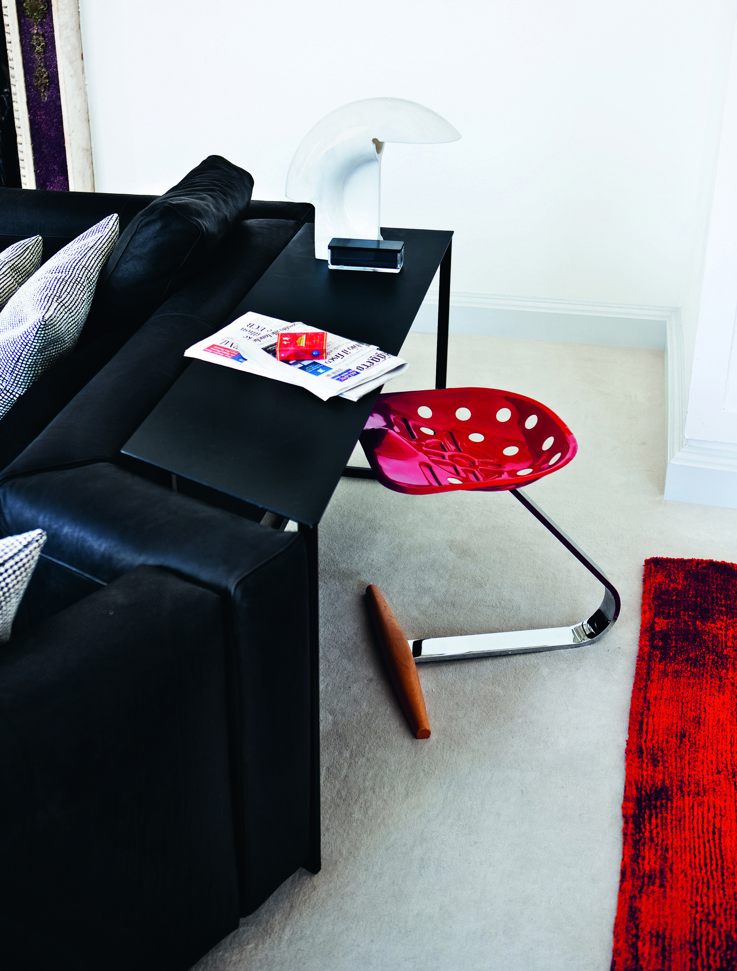 Roter Mezzadro Hocker von Zanotta mit Traktorsitz neben schwarzem Sofa und Beistelltisch.