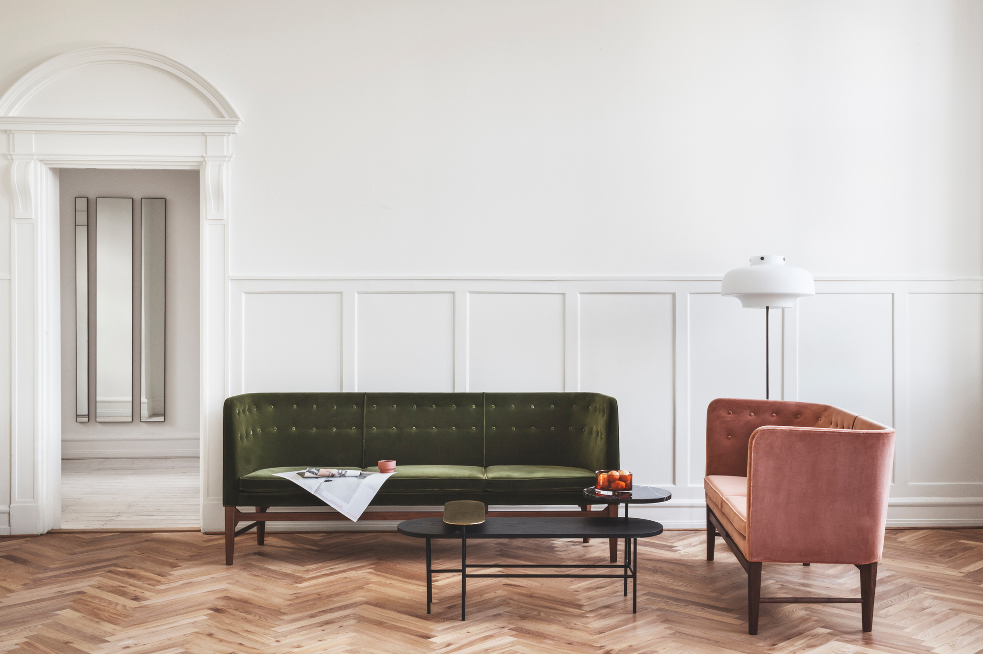 Wohnzimmer mit grünem AndTradition Mayor Sofa, rosa Sessel und schwarzen Couchtischen auf Parkett.