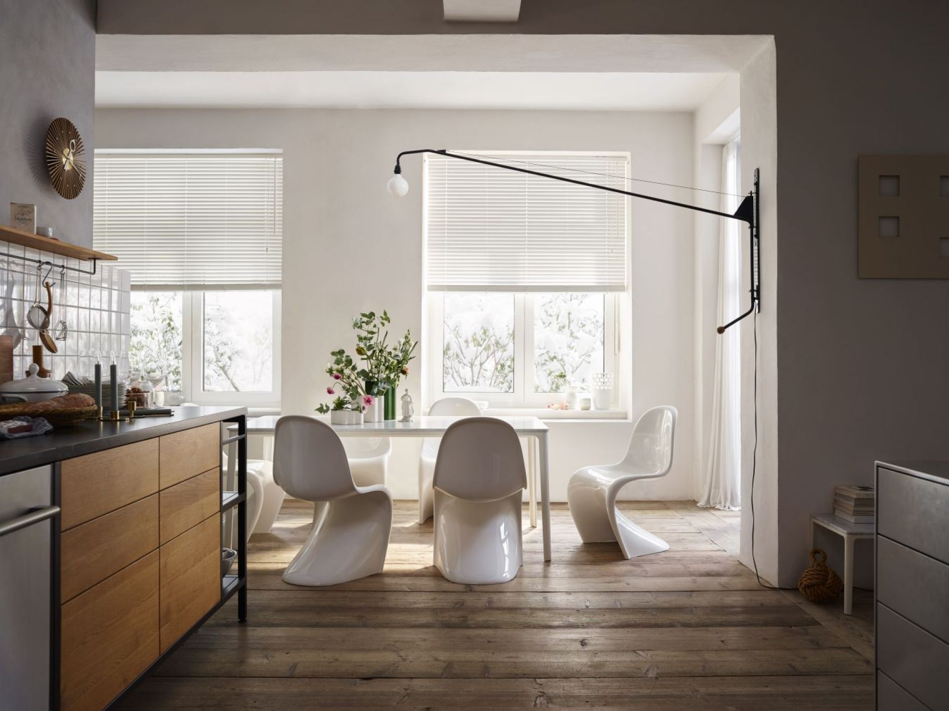 Helle Küche mit weißen Jalousien vor Fenstern, Esstisch mit weißen Panton Stühlen und Holzboden.
